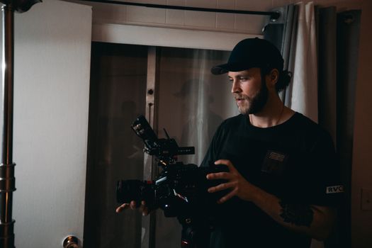 Bearded man filming with professional video camera indoors, showcasing filmmaking in action.