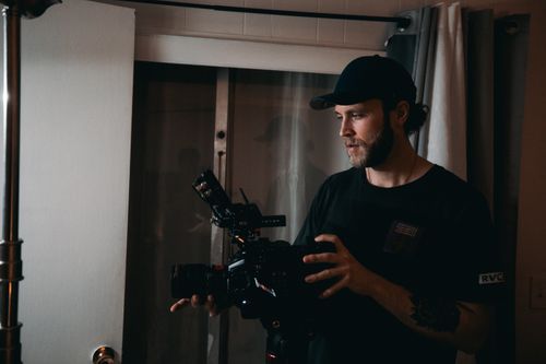 Free Bearded man filming with professional video camera indoors, showcasing filmmaking in action. Stock Photo