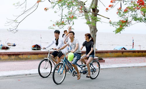 Zwei Jungen Und Ein Mädchen, Die Fahrräder Auf Der Straße Neben Dem Gewässer Fahren