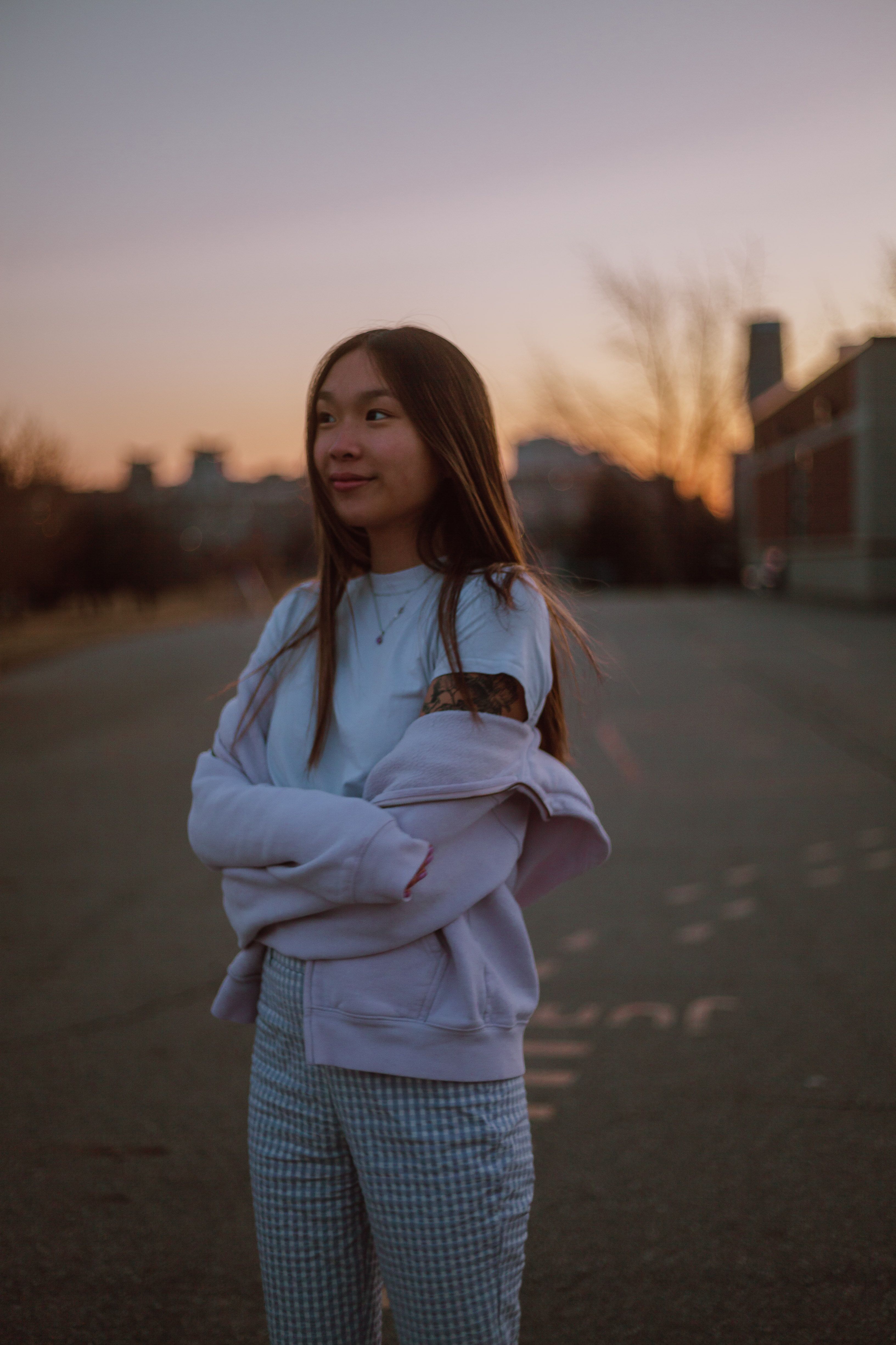 Young woman with arms crossed standing in urban area at sunset.