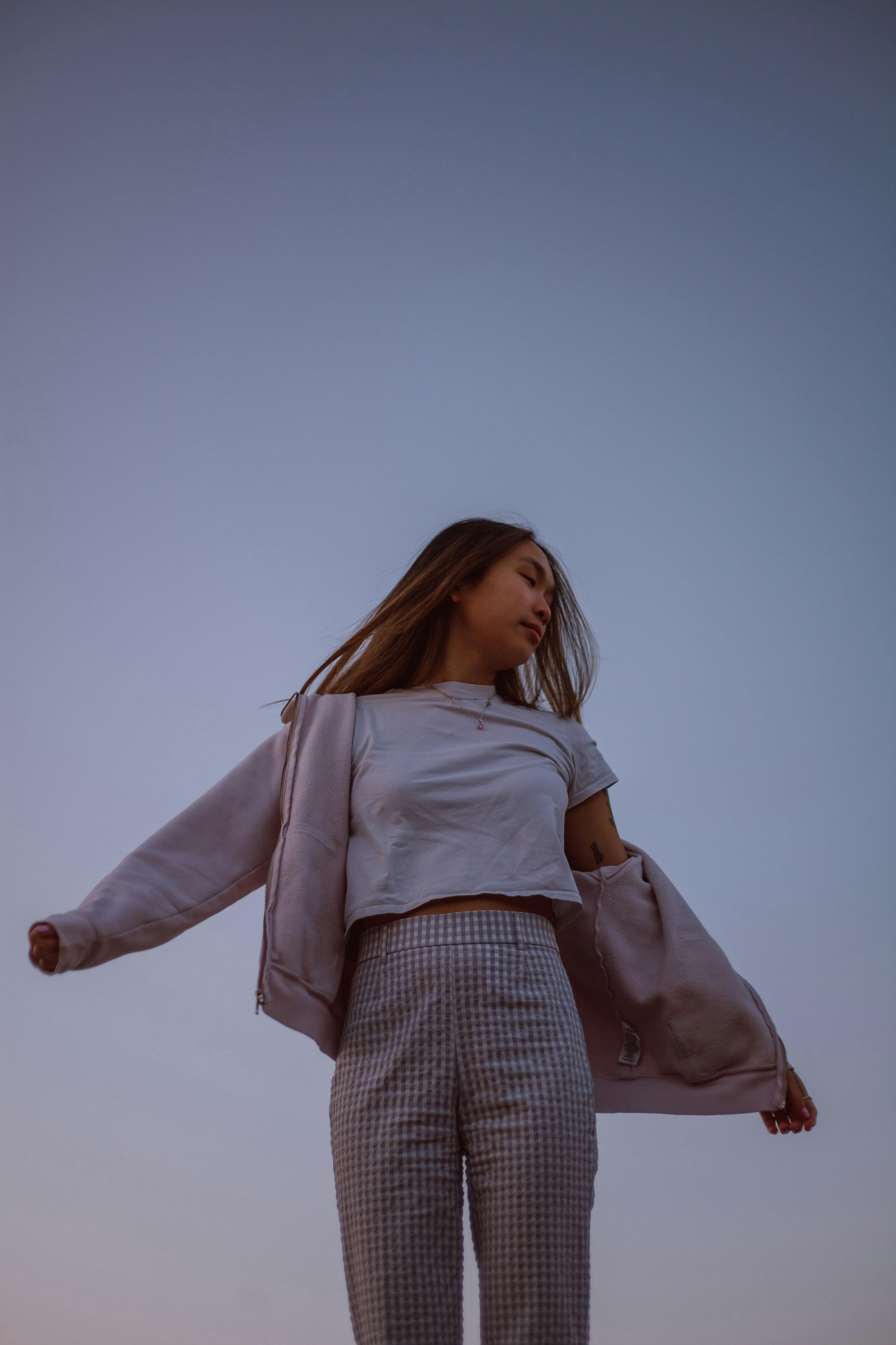 Young woman in casual clothes with arms open against a twilight sky, depicting freedom and serenity.