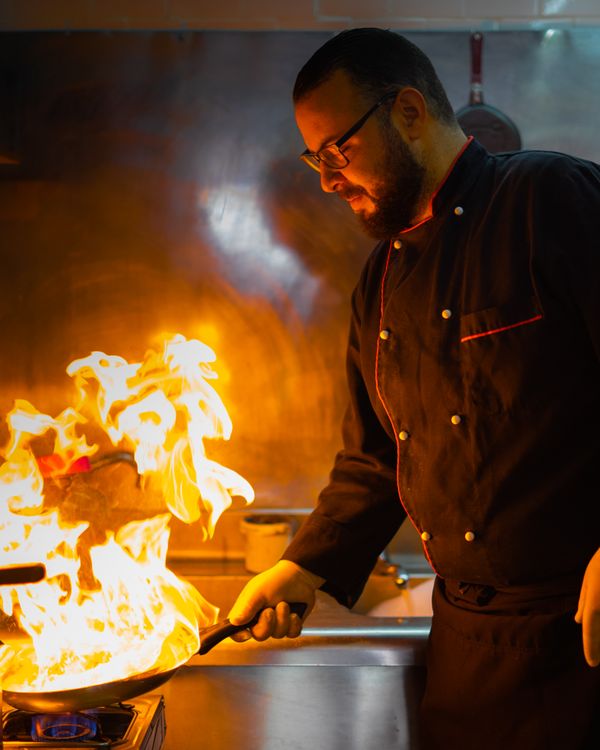 How Much Does a Chef Earn in India? Role-by-Role Salary Breakdown (2026) 2 Professional chef expertly managing a flaming pan in a commercial kitchen, demonstrating high-heat culinary technique.