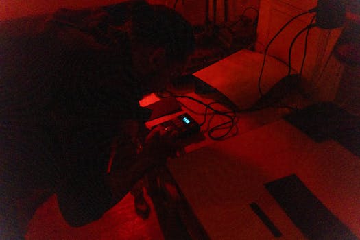 A photographer works in a red-lit darkroom, processing film photography.
