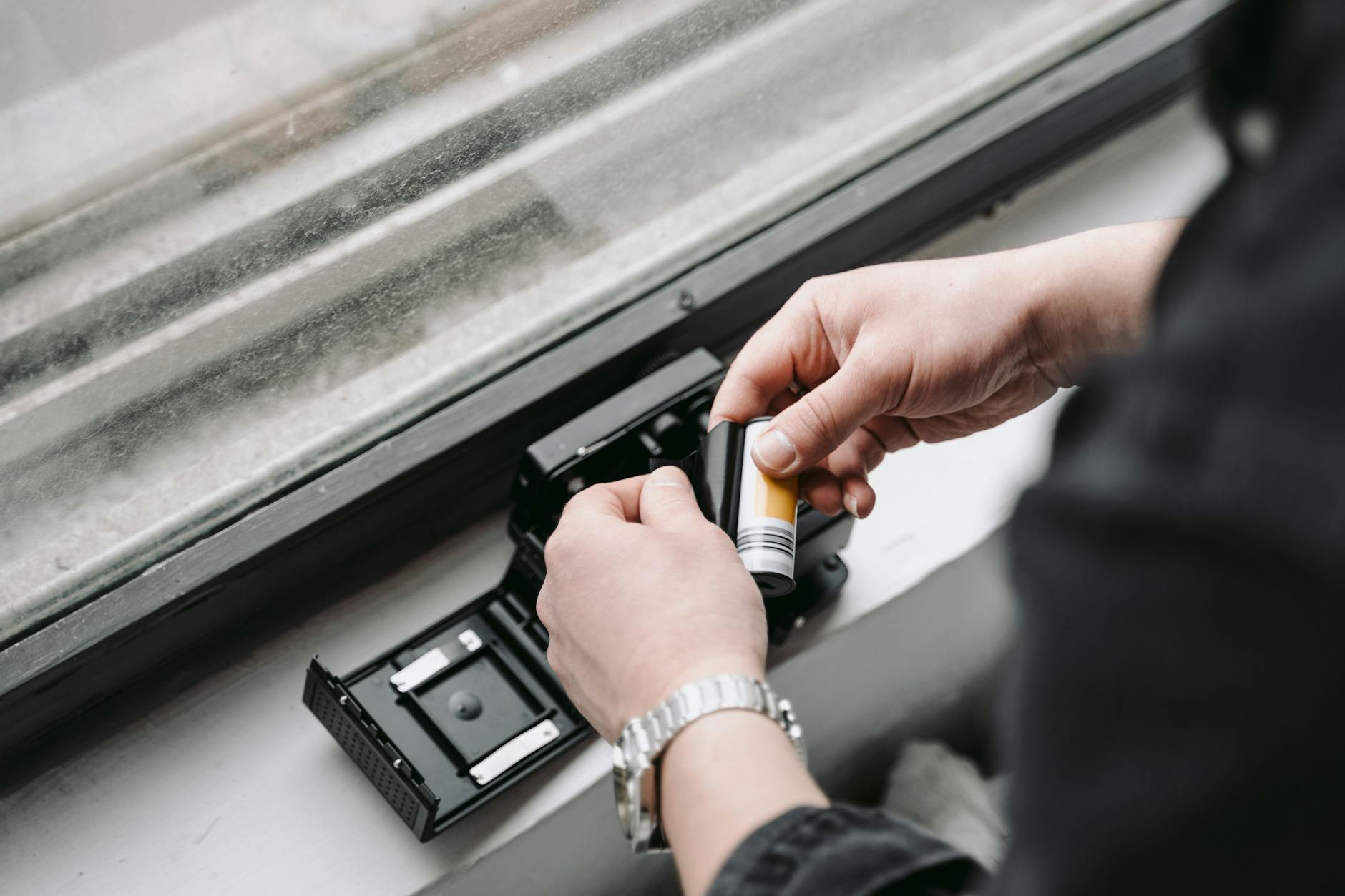 Hands loading camera film into a vintage camera by a window
