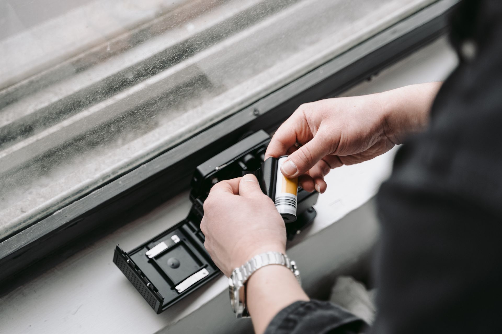 Hands loading camera film into a vintage camera by a window, showcasing classic photography.