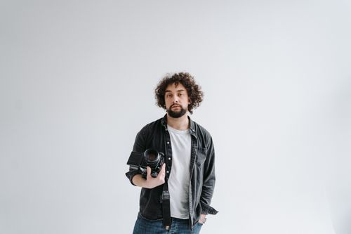 Free Photographer in studio setting holding professional camera against white background. Stock Photo