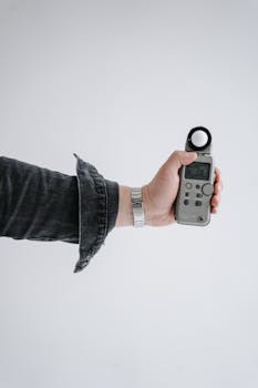 A person's hand holding a light meter against a plain white background.
