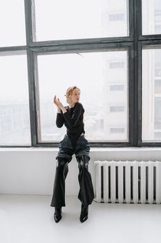 Stylish woman in modern outfit posing by a large window in a bright indoor setting.