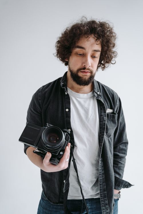 Free Portrait of a bearded male photographer holding a professional camera in a studio setting. Stock Photo