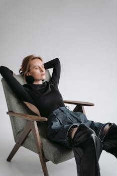 A young woman in black clothing relaxes in a modern armchair, eyes closed.