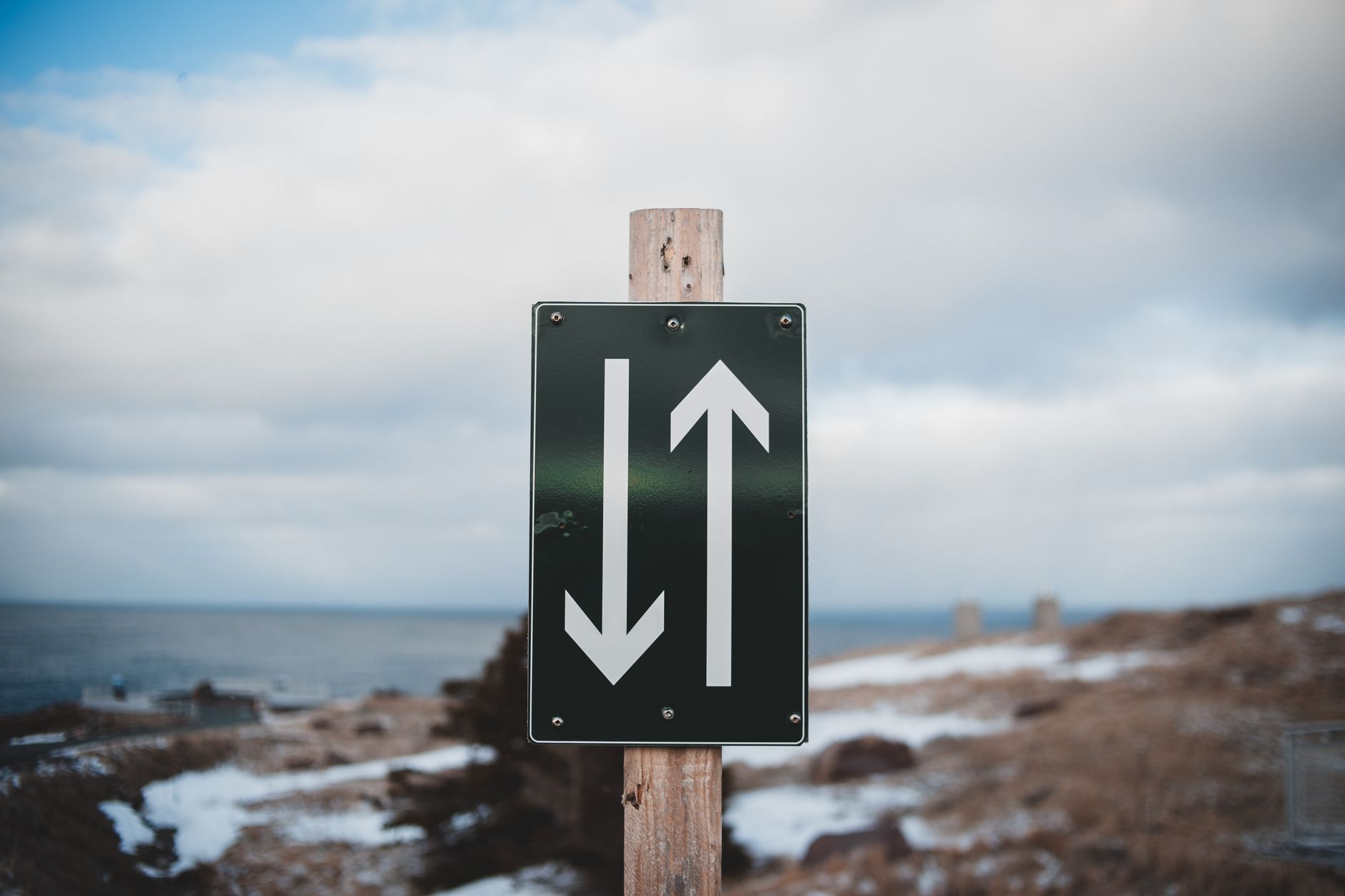 Sign of two way trail on sandy shore of calm sea with snow under cloudy sky on winter day