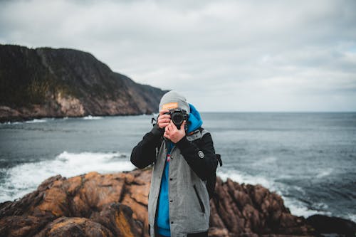 Free Young male photographer taking pictures on camera on rocky seashore Stock Photo
