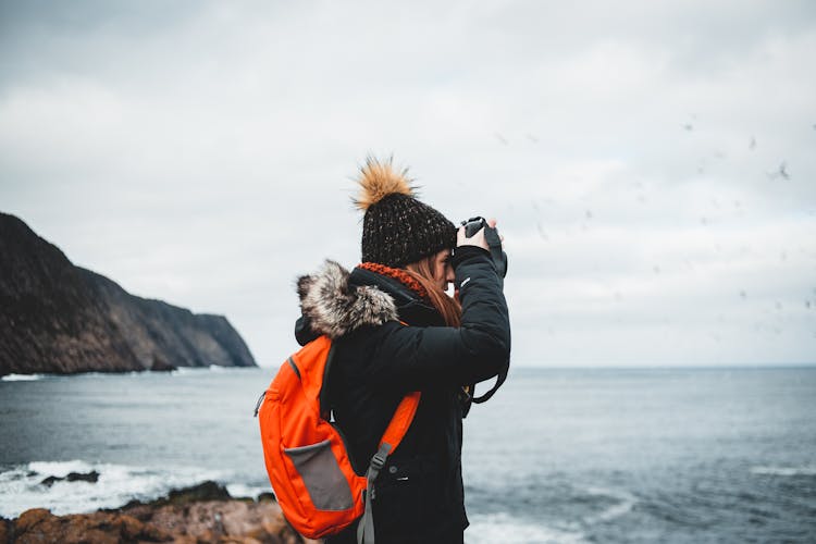 Young Female Hiker Shooting Ocean Against Gloomy Sky