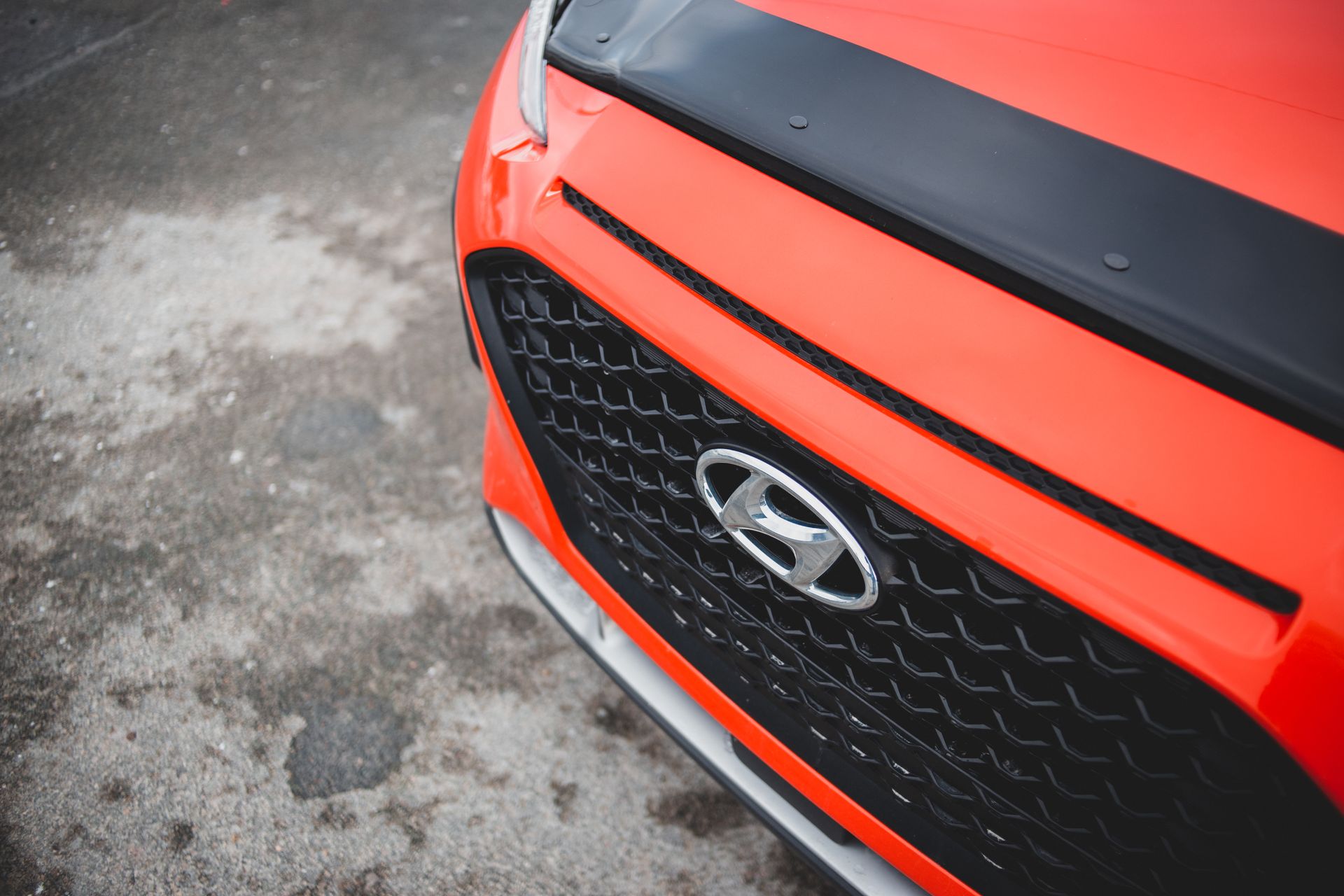 From above of bonnet of modern red car with radiator grill parked on asphalt road on rainy day