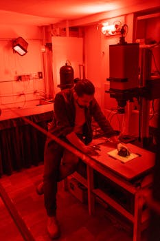 Photographer processes film in vintage darkroom with red lighting.