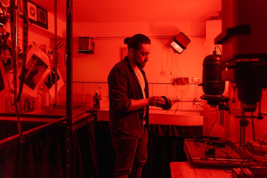 A man working in a red-lit darkroom developing film using traditional equipment.
