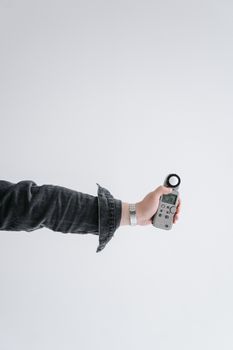 A close-up shot of a hand holding a digital light meter against a white background, highlighting photography equipment.