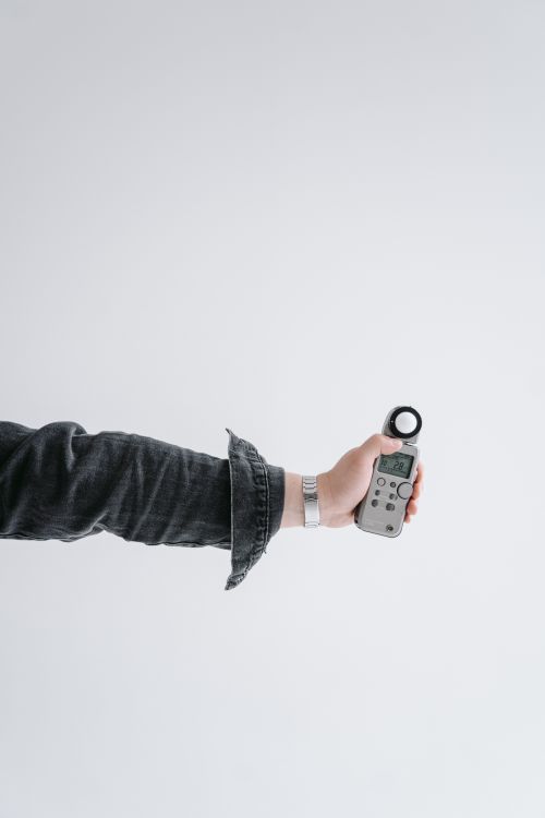 Free A close-up shot of a hand holding a digital light meter against a white background, highlighting photography equipment. Stock Photo