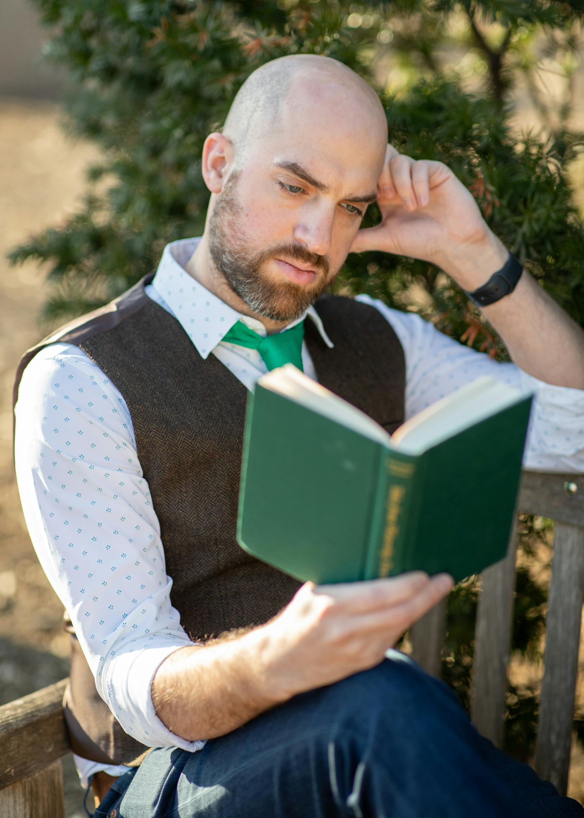 bearded bald man sitting on bench and reading book