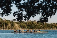 Anonymous athletes in boats with oars practicing canoeing sport on rippled lake against green trees in daytime
