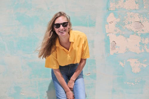 免费 女人穿着黄色polo衫站在蓝绿色的混凝土墙前 素材图片