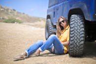 一名女子戴着太阳镜，在沙漠中对着蓝色越野车放松身心