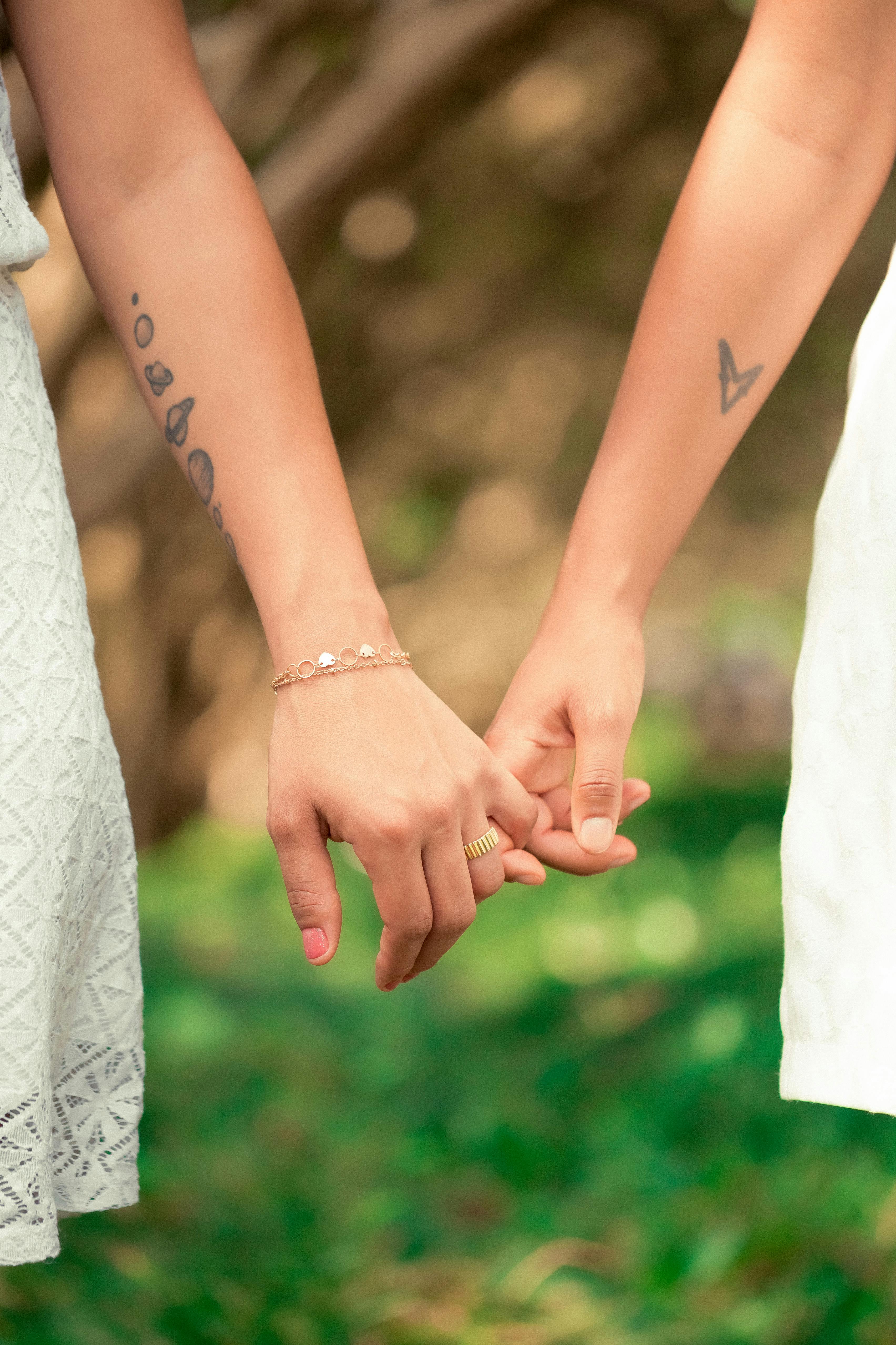 Free Crop unrecognizable girlfriends holding hands on blurred background of fresh verdant grass in park Stock Photo