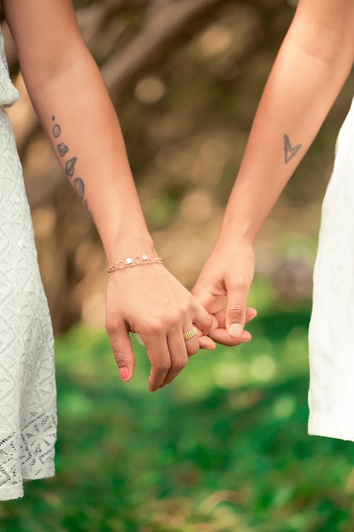 Crop unrecognizable girlfriends holding hands on blurred background of fresh verdant grass in park