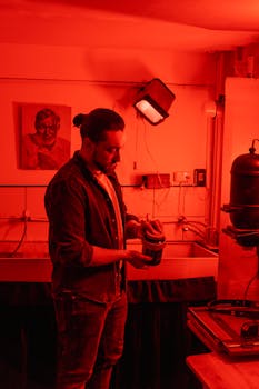A photographer working in a red-lit darkroom, processing film in a development tank.