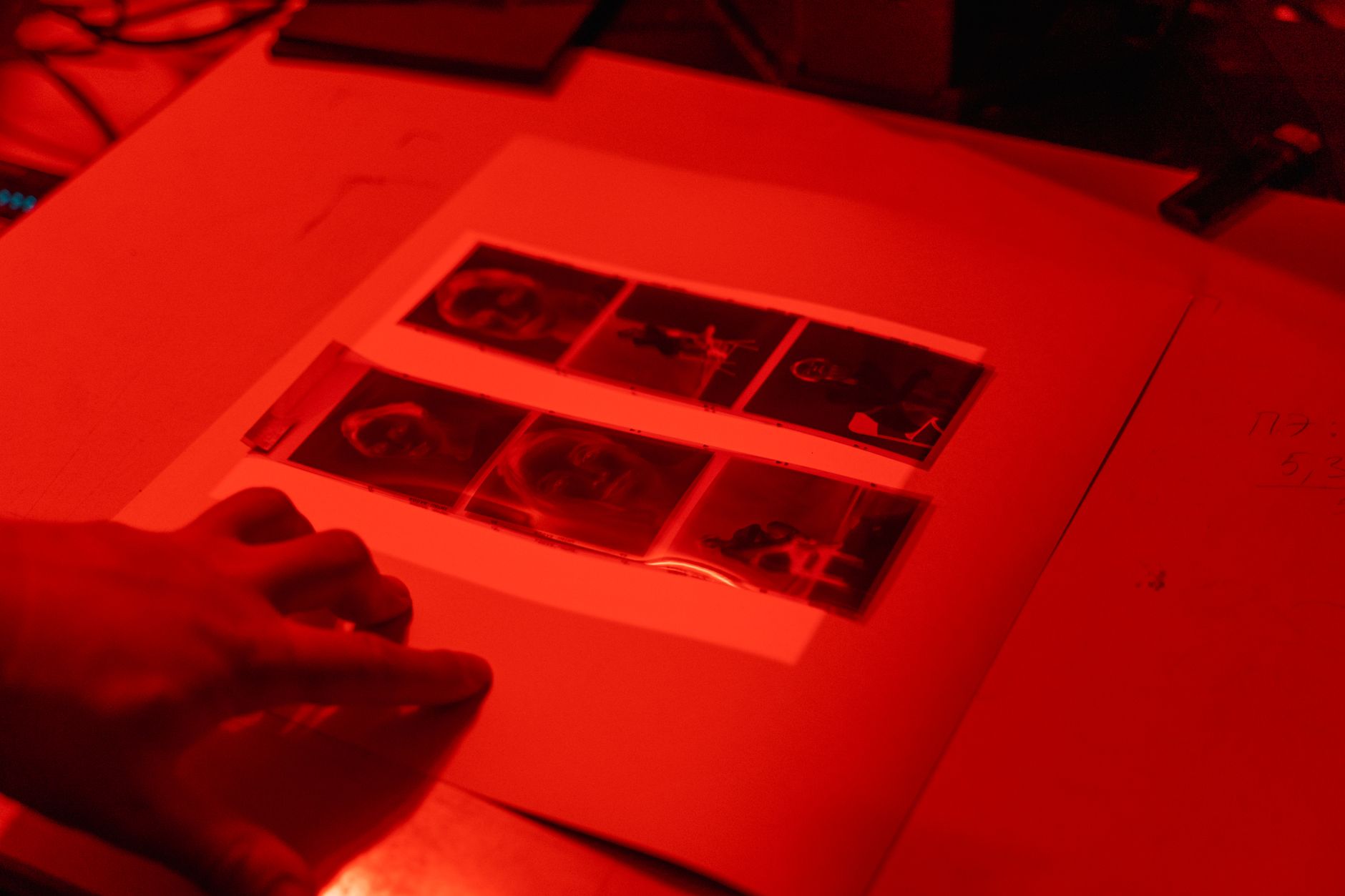 A hand inspects photographic negatives in a dimly lit darkroom.