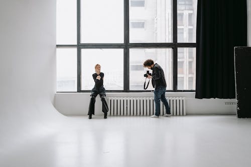 A Photographer Taking Photo of a Woman Sitting Beside the Window