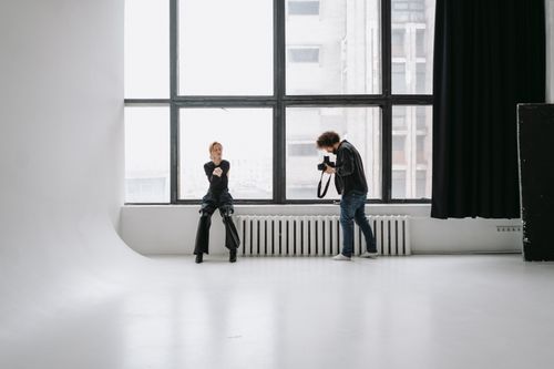 Free Photographer capturing model in modern studio with large windows and minimal decor. Stock Photo