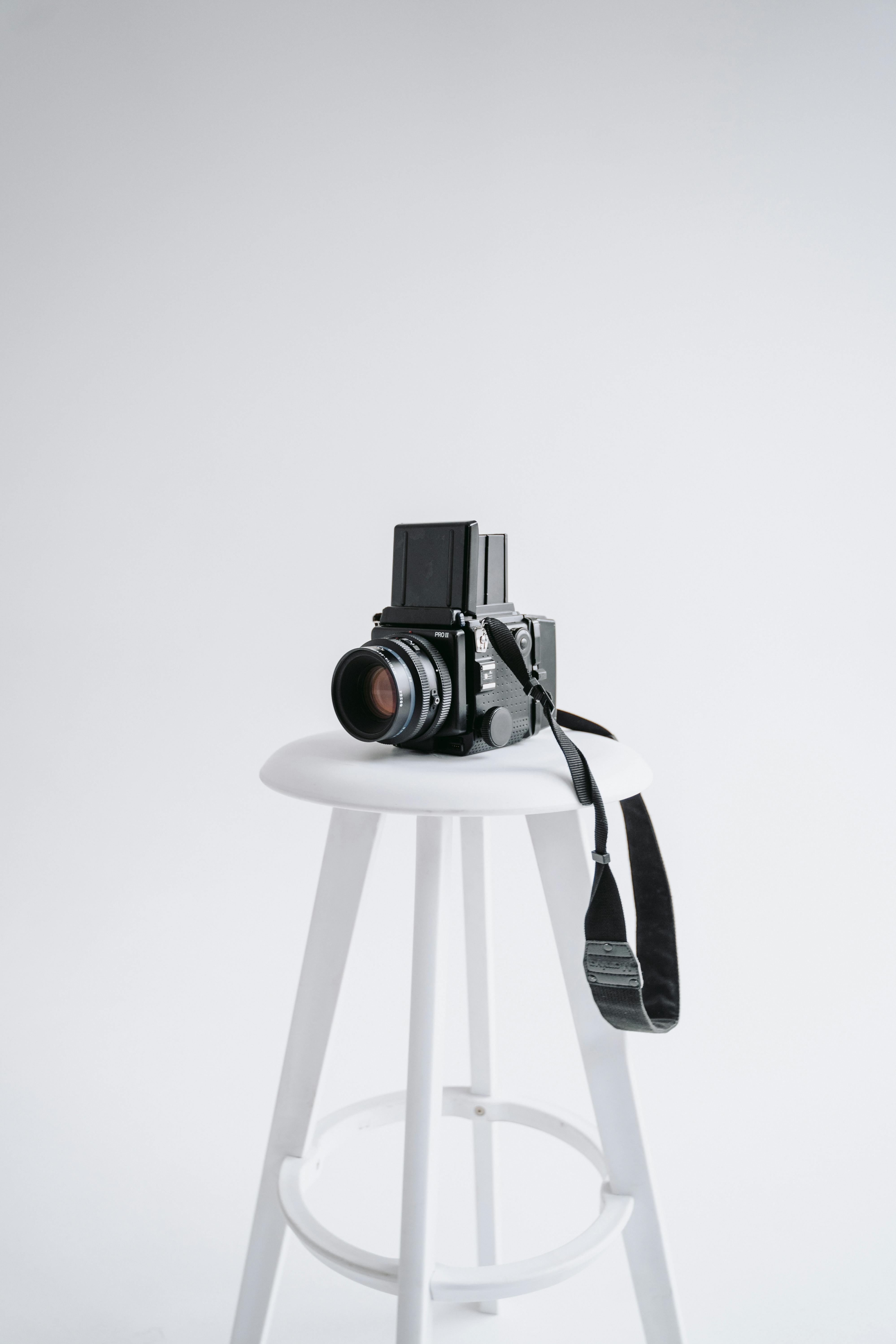 A vintage camera placed on a modern white bar stool in a minimalist studio setting.