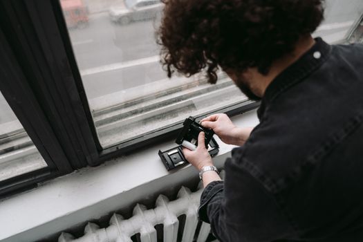 Person handling a film cartridge by a window sill, capturing a candid moment indoors.