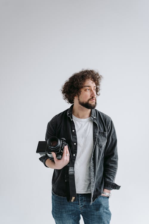 Man Looking Afar While Holding a Black Dslr Camera 