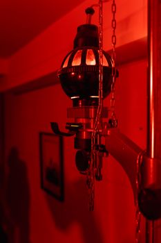 Close-up of an antique darkroom lamp with chains, under red light illumination.