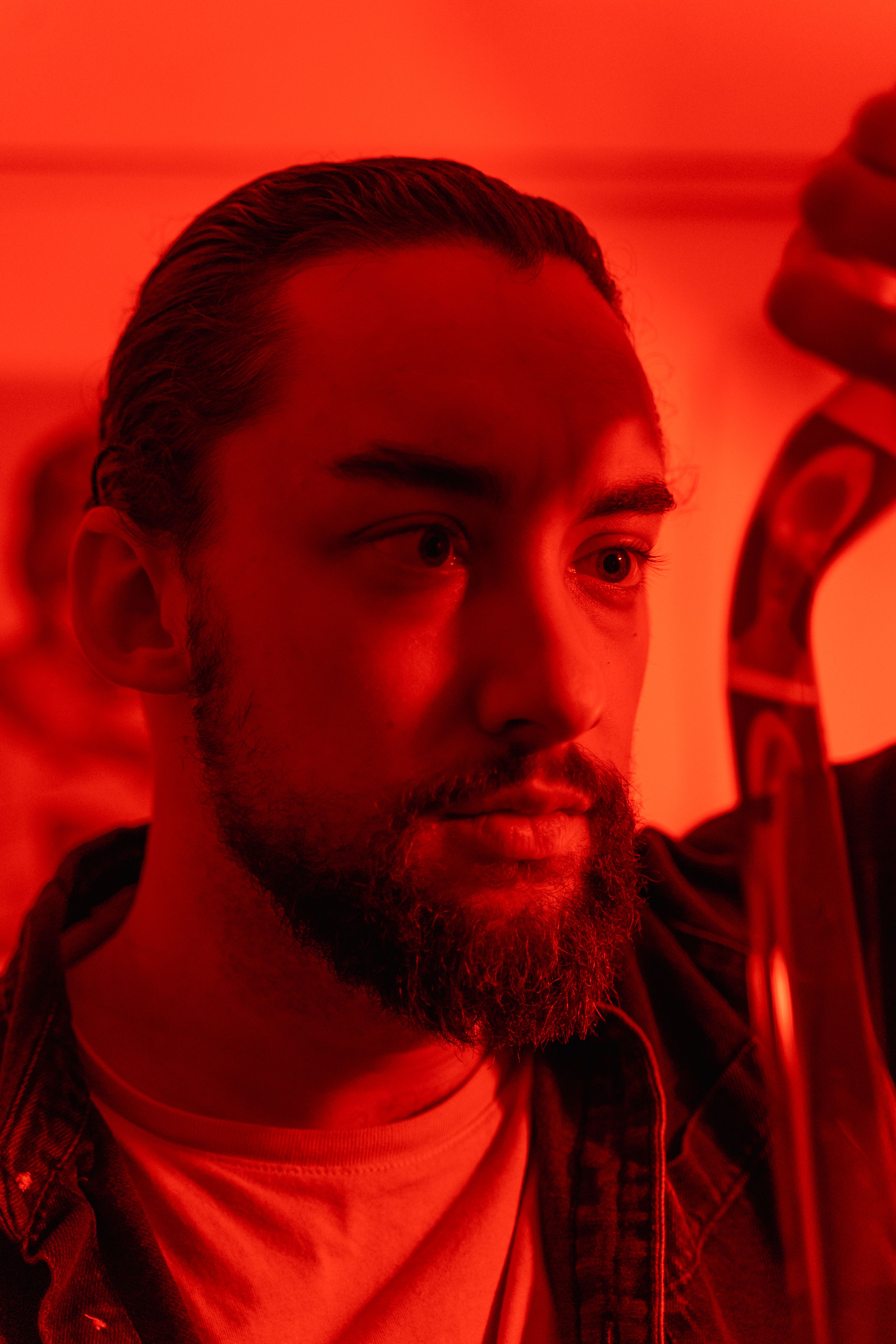 A contemplative man inspects a film strip in a darkroom with red lighting.