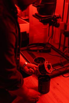 Photographer developing film in a dimly lit darkroom under red light.