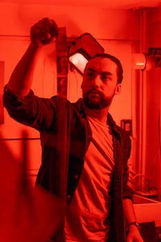 Man working in a darkroom holding film negatives in red lighting environment.