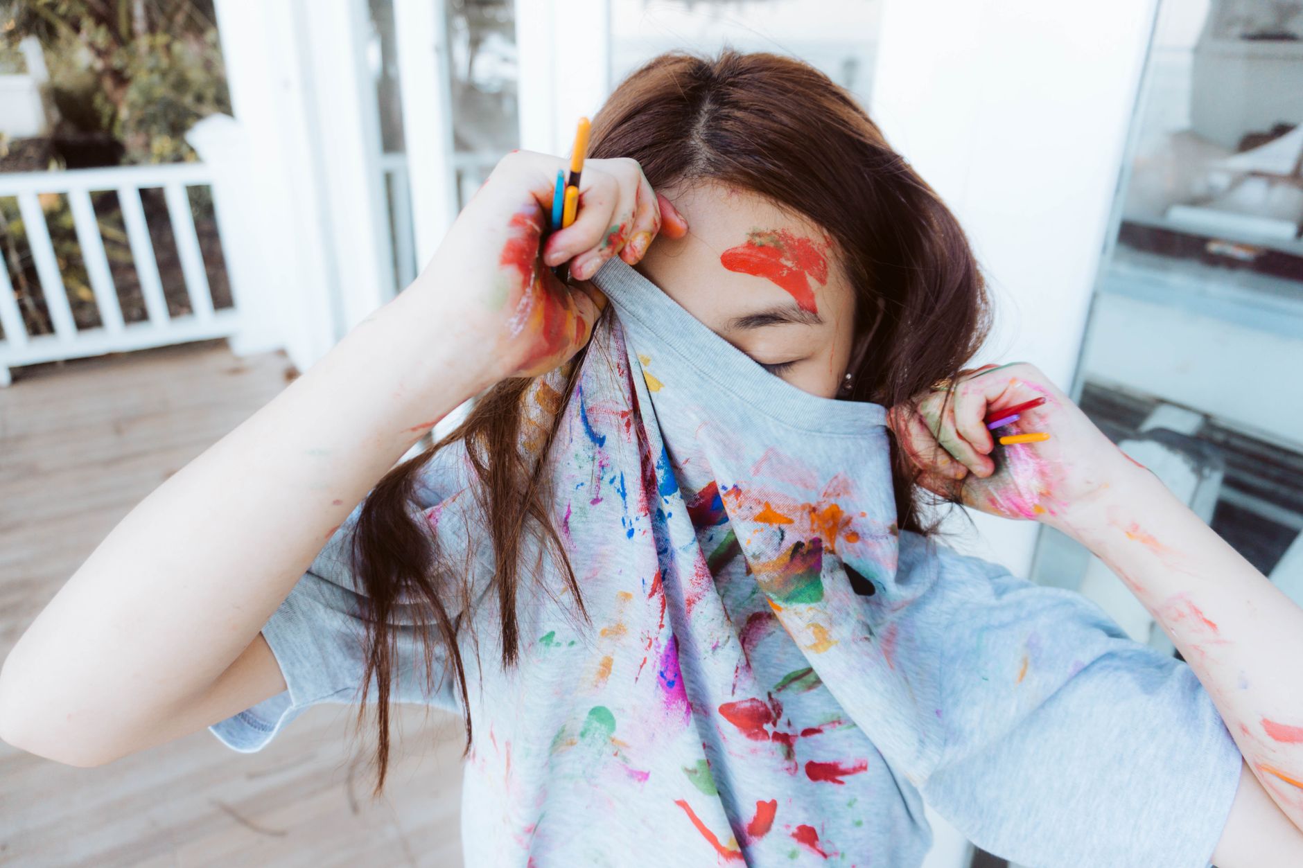 A playful artist covered in vibrant watercolors, hiding face with a colorful shirt.