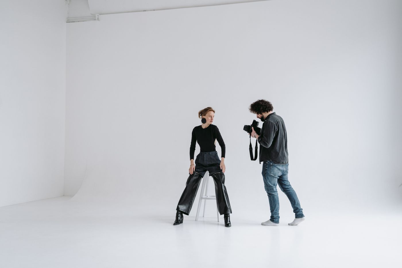 Fotograf arbetar med en sittande modell framför vit studiobakgrund.