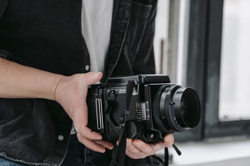 Free Close-up of a person holding a vintage medium format camera, indoors, with a focus on hands and camera details. Stock Photo