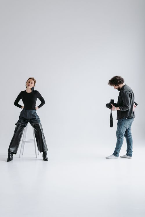 Free A professional photographer capturing a seated model during a studio photoshoot with a white background. Stock Photo