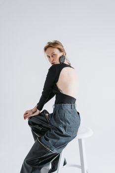 Stylish woman in modern outfit sitting and posing on stool in a studio setting.