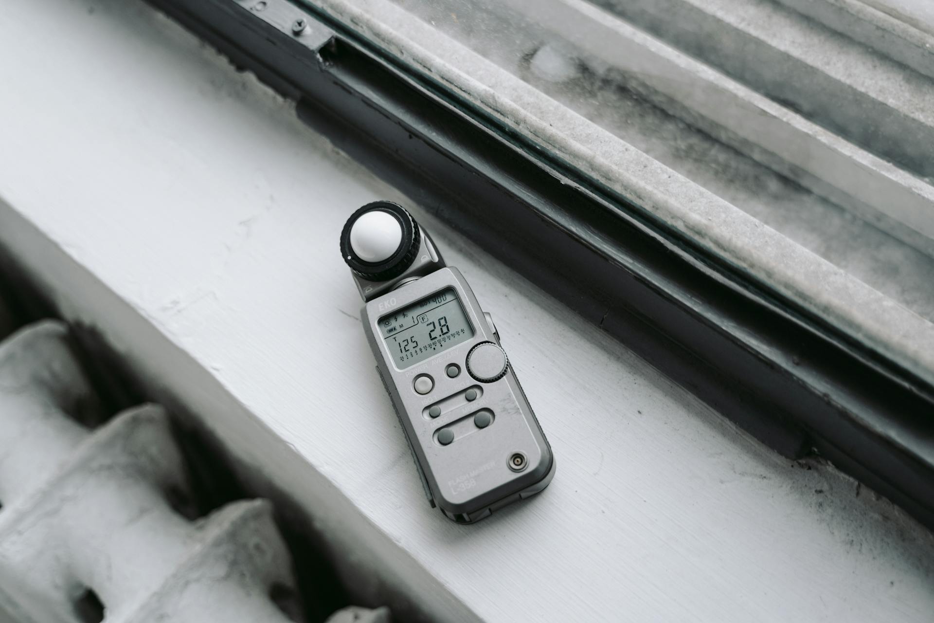 A close-up of a digital light meter placed on a windowsill, emphasizing modern photo equipment.