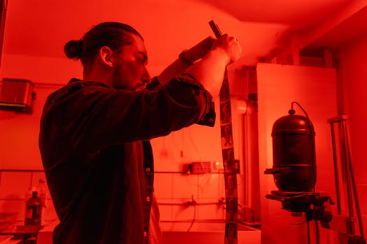 Photographer works with film negatives in a red-lit darkroom for traditional photographic processing.