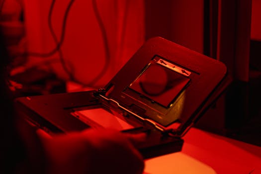Film photo development in a red-lit darkroom showcasing hands handling equipment.