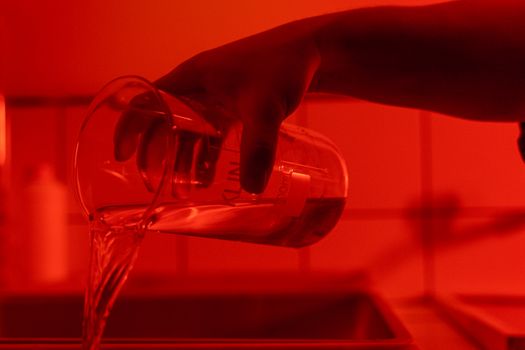 A hand pouring liquid from a beaker under atmospheric red lighting indoors.