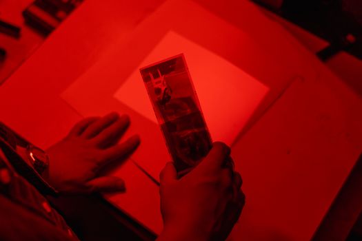 A detailed view of a film strip being handled under red light in a darkroom.