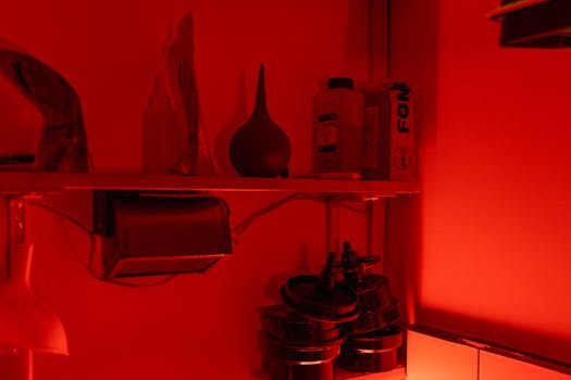A vintage darkroom illuminated with red light featuring photography equipment on shelves.
